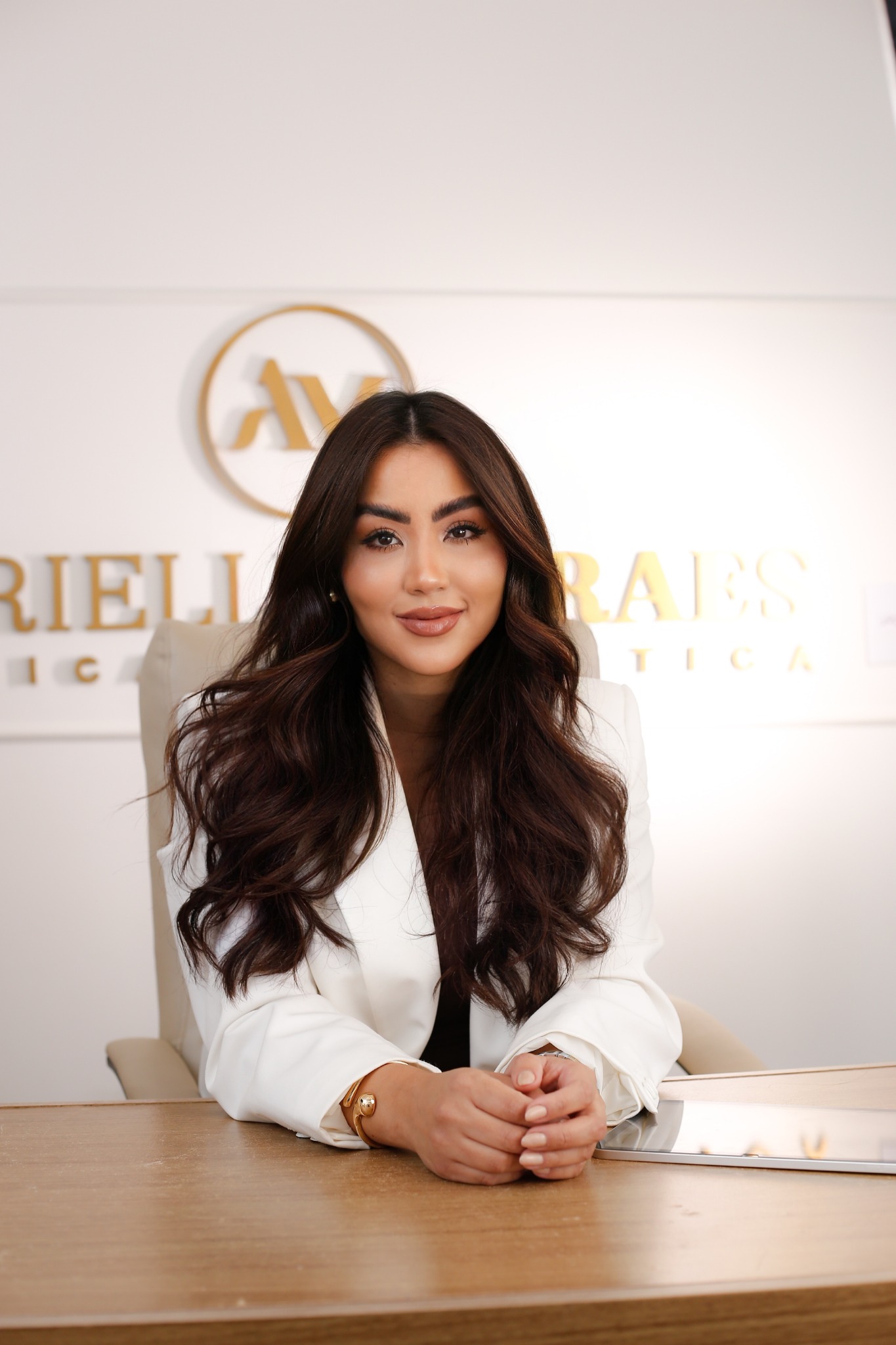 Adrielle Moraes sentada à mesa na clínica, com a marca ao fundo